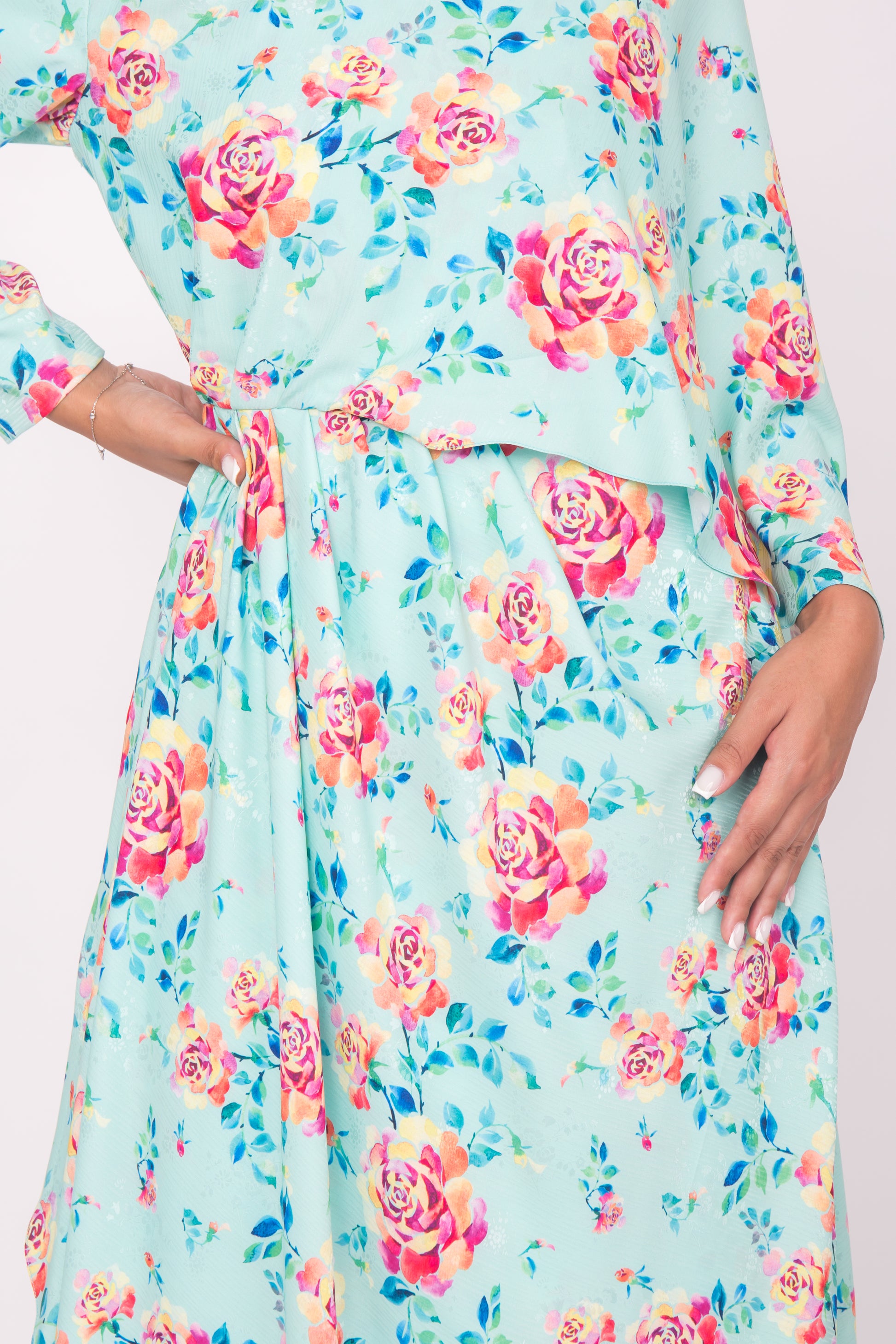 Close up shot of an aqua floral printed silk dress, posing against white background.